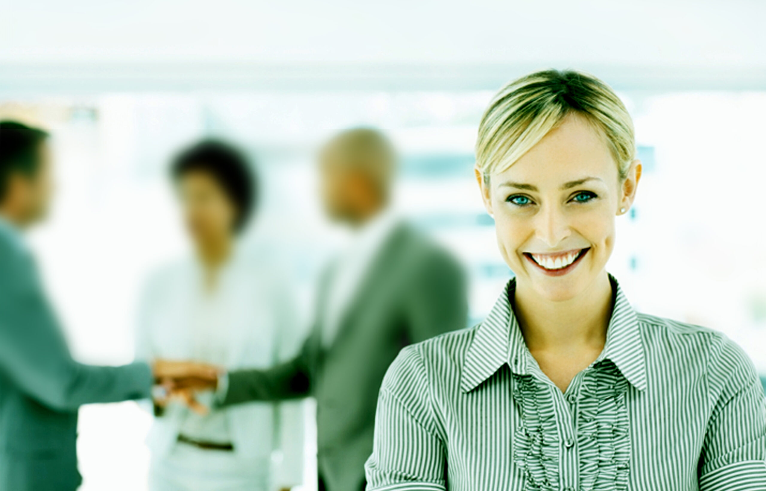 Smiling female paralegal or legal professional in a striped collared shirt standing in front of colleagues shaking hands in a bright office context.